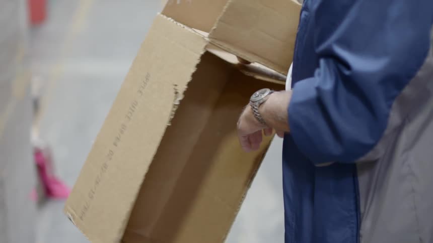 Warehouse worker tears a cardboard box with his hands