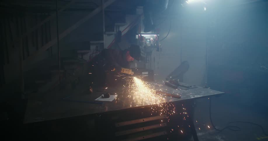 Sparks fly while a man uses a power tool in a workshop