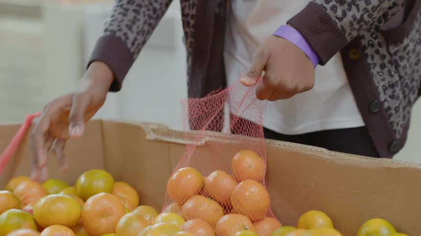 A person placing fruits in a mesh bag