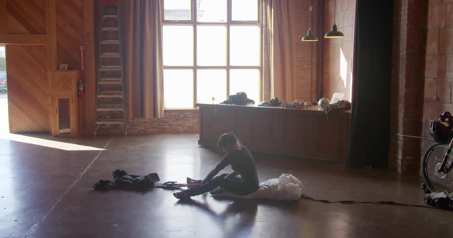 A woman sits on the floor in a large building pulling the rope of an object closer to her