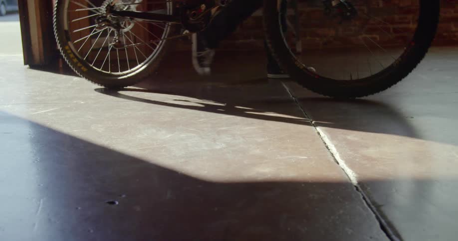 A woman walks her bicycle into a building and throws climbing rope on ground