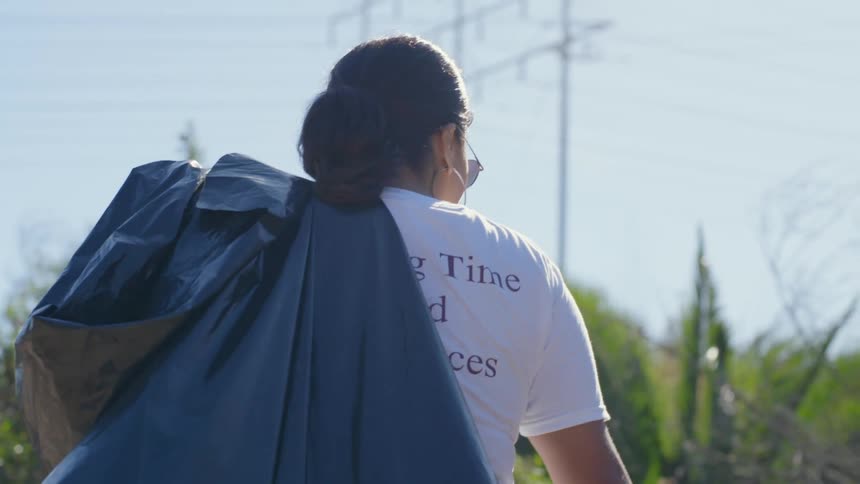 A woman walking outdoors while carrying a plastic trash bag