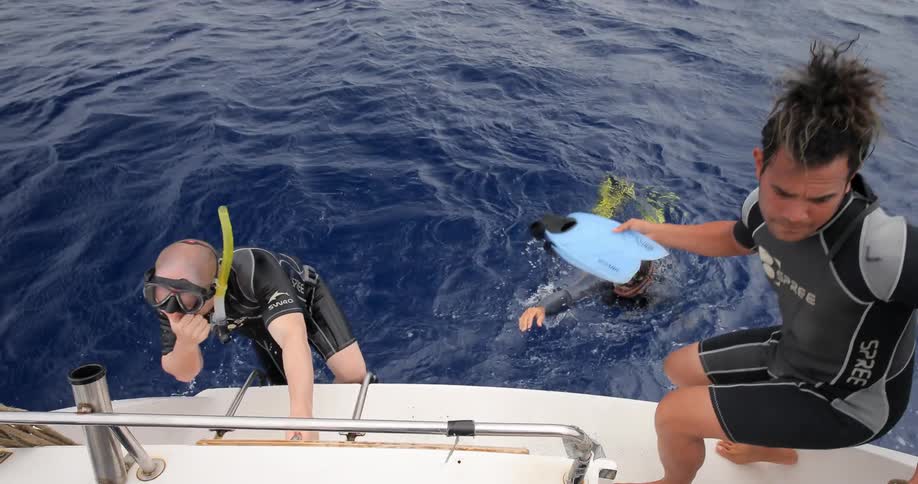 Snorkelers climb onto a boat after having swam in the ocean