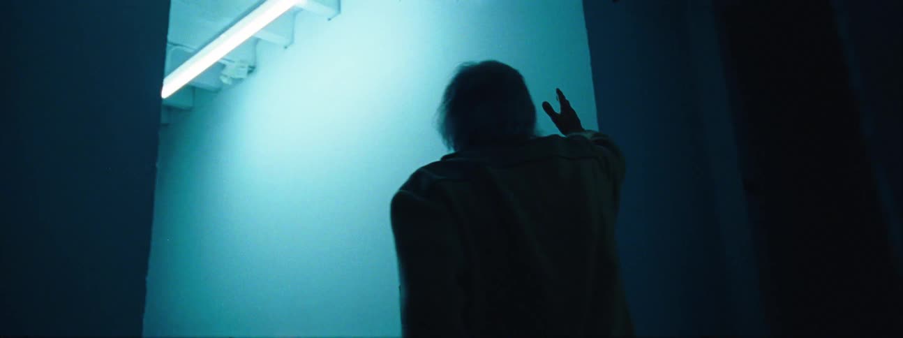 Man enters a lit room and leans his body against the wall