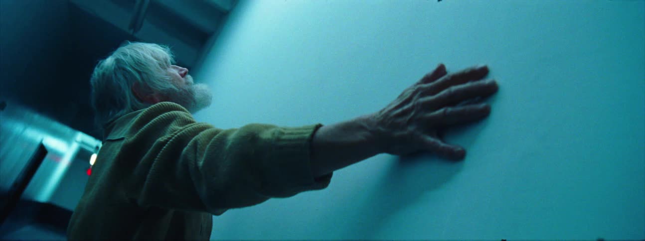 Elderly man clutches onto wall in dimly lit corridor