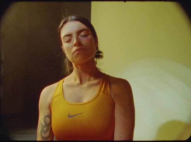 Woman stands with eyes closed stretching her neck among lights and shadows
