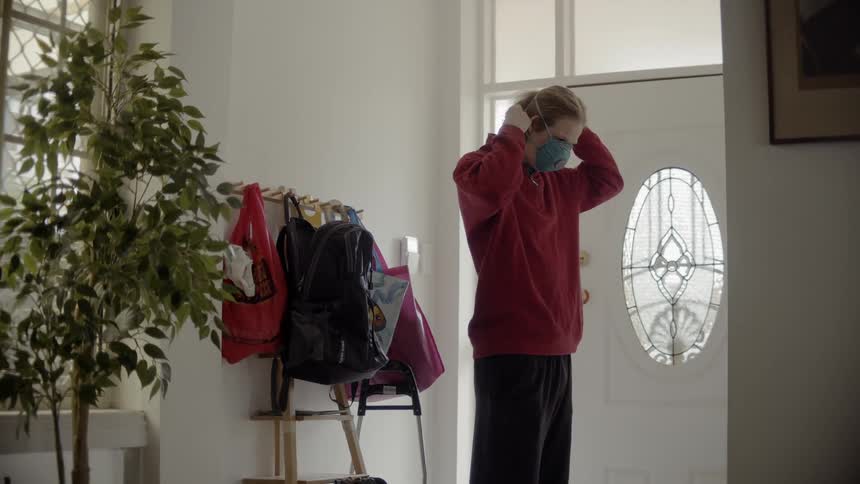 A person puts on a medical mask standing inside by their door