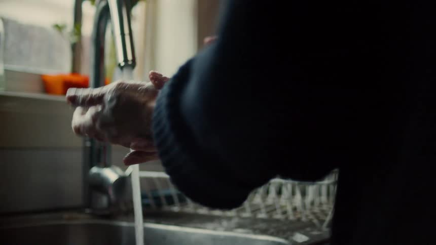 Two people wash their hands in a kitchen sink