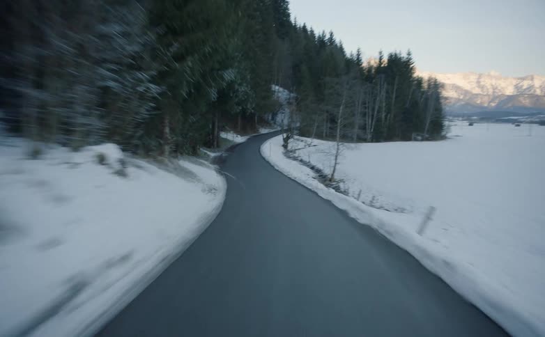 Vehicle drives along winding narrow road in the snowy hills