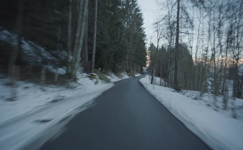 Driving down asphalt road bordered by snow covers forest and slopes