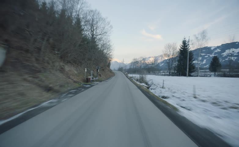 A road at the bottom of a hill next to a field covered in snow