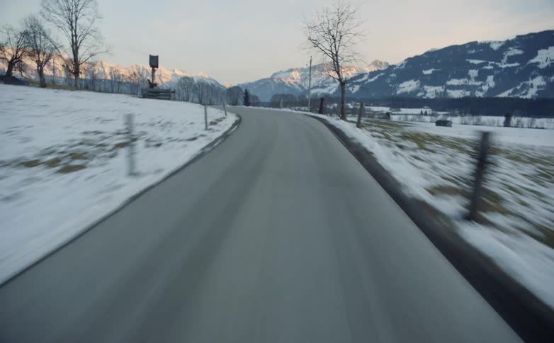 Jesus on the cross in a small wooden shelter on the side of a curving rural road with snow covered fields and mountains on the horizon