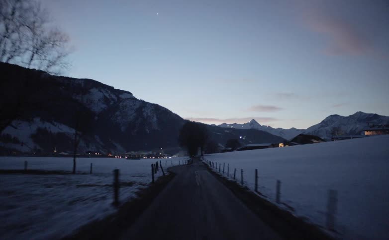 A narrow road through a snowy countryside leading towards a small town
