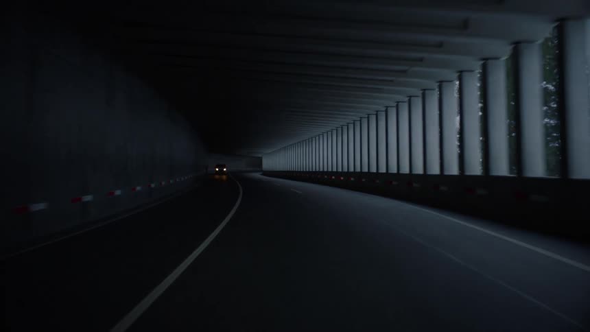 Vehicle travels through tunnel bordering snow covered mountain slope