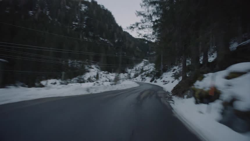 Vehicle drives along winding narrow road in the snowy mountains