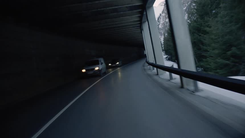 Traveling down freeway under enclosure past traffic and snow and forest covered mountains