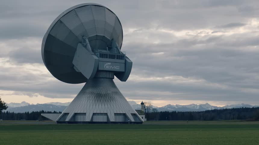 A large satellite dish in a large field on a cloudy day