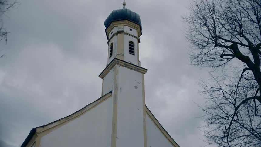 A steeple on a small church on a cloudy day