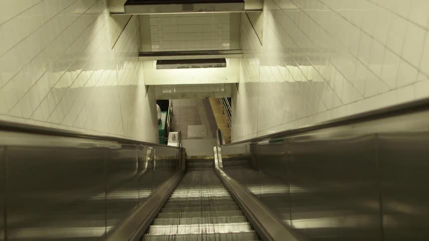 A descending escalator leads to an empty subway platform