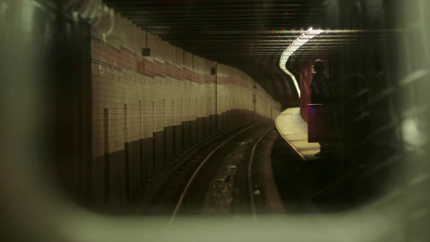 Empty tracks and subway platform with only one person standing there seen through the rear window of a train