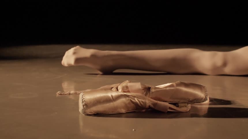 A person is stretching their leg near a ballet shoe