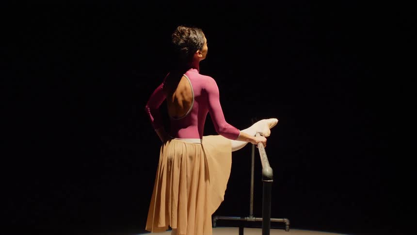 Ballerina stretches her leg at ballet barre on the stage