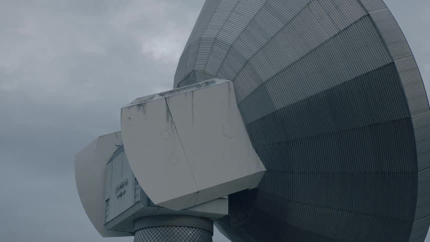 Radio telescope stands tall under cloudy sky near buildings