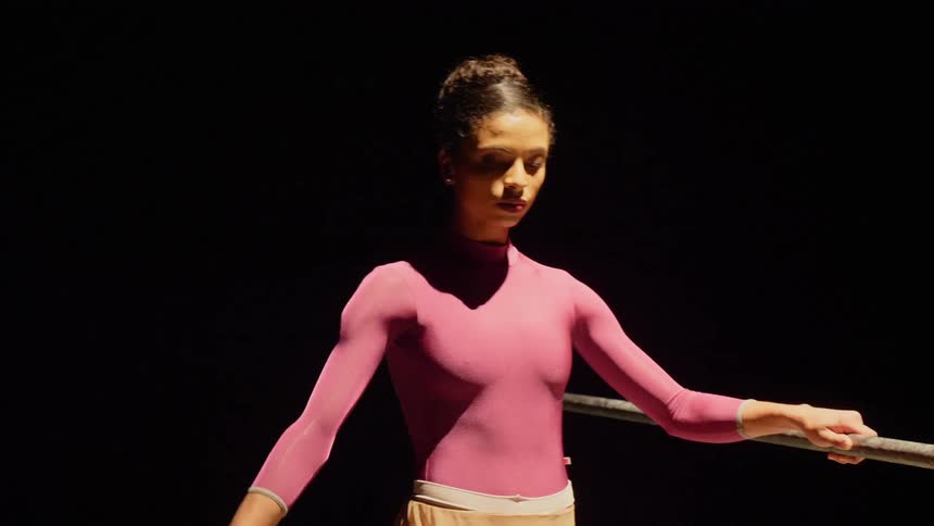 A woman holding onto a ballet barre while dancing and raising her leg