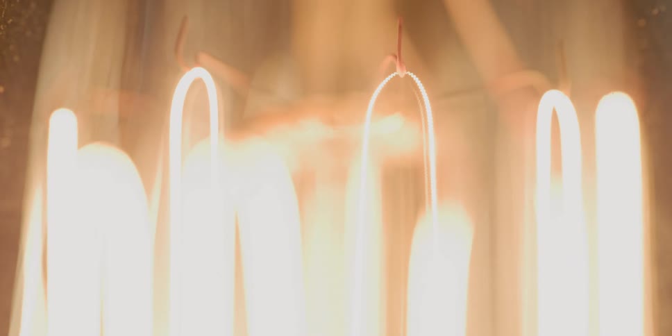 The filaments of a bulb glow orange then shine bright before dimming