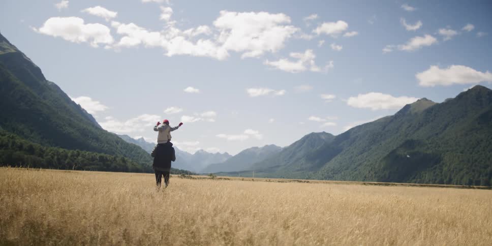 Man carries son on his shoulders in the dry field on a sunny day