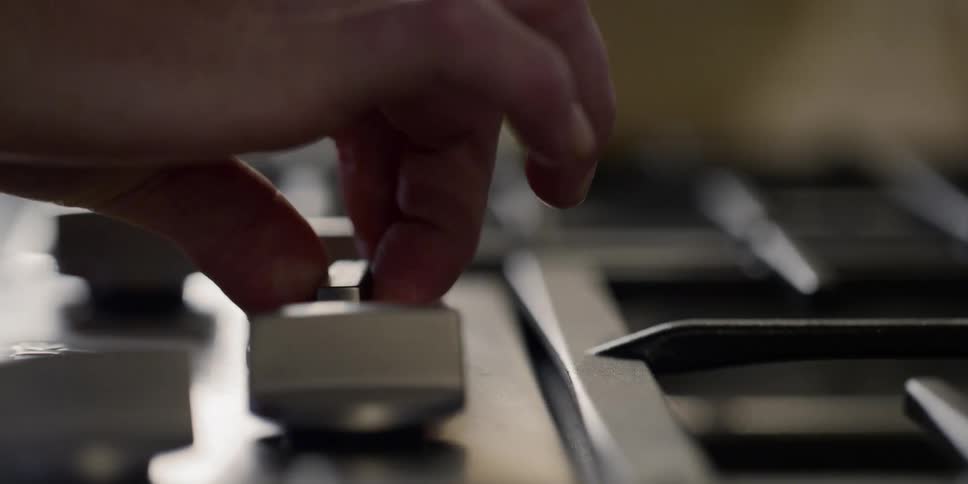 A hand turns the stove top burner on