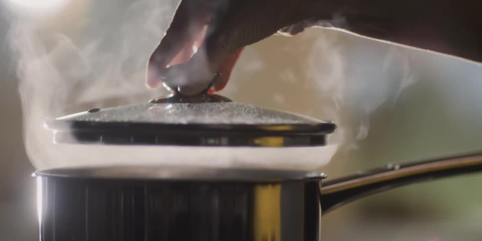 Female covers a steaming pot with glass lid that is dripping with condensation