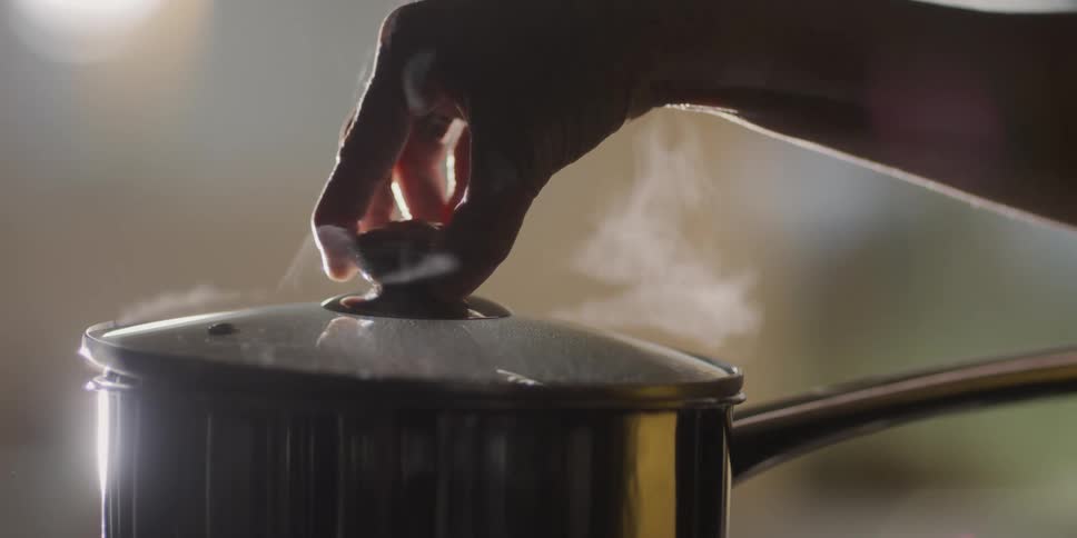 Womans hand opens the lid of the pot in the kitchen