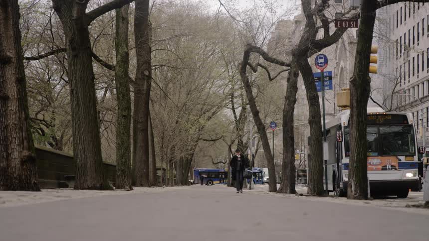 Buses and cars drive down a city street as a person walks along the sidewalk