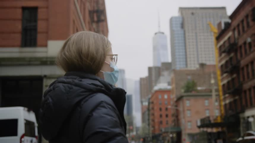 Woman wearing face mask stands on the corner in city downtown