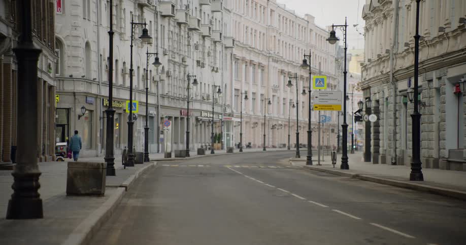 A single pedestrian walking down an otherwise empty city street lined with white buildings during the day