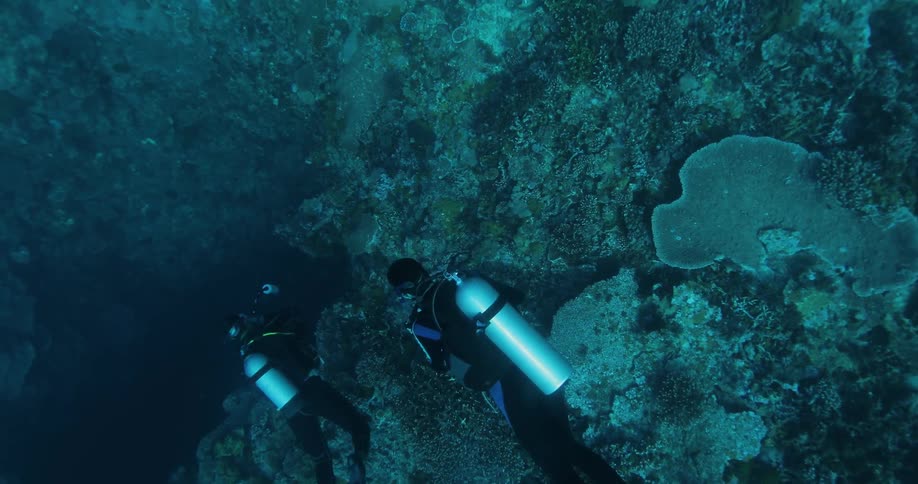 Two men scuba dive over a dark underwater cave