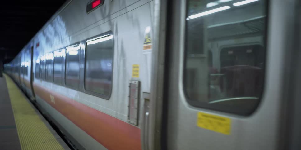 The conductor leaning out the window of the commuter train as it leaves an empty station with only one passenger on board