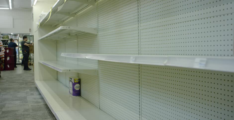 People stand at the end of an empty shelf in a store