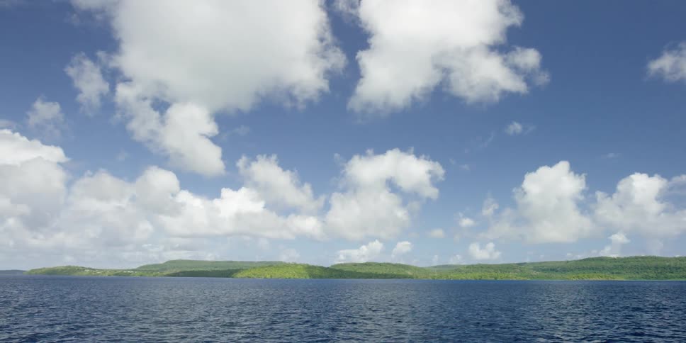 Fluffy clouds float over green hills and a body of water