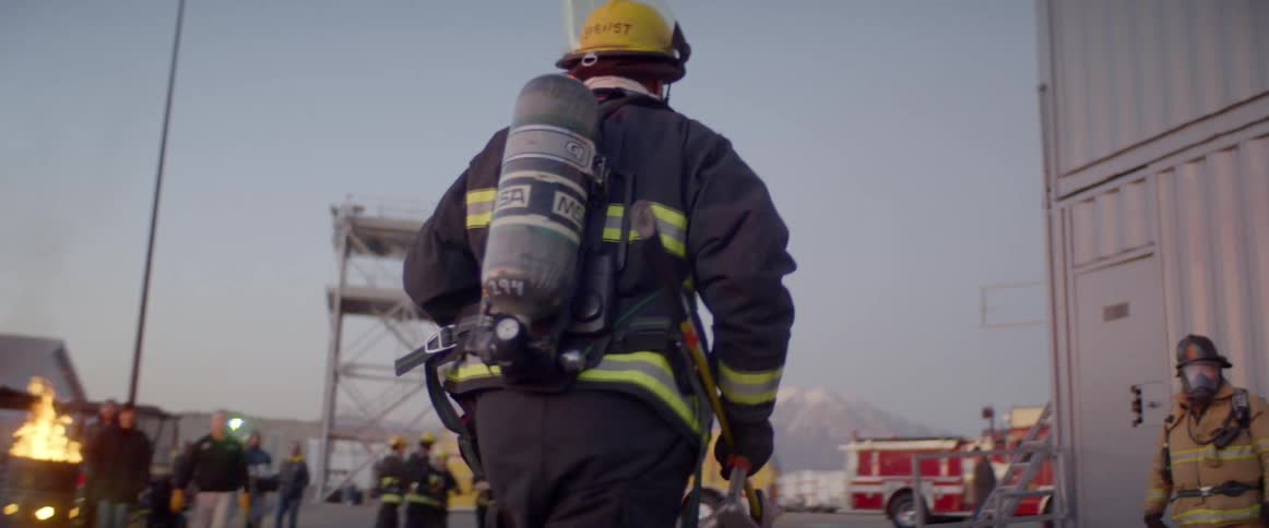 Fireman runs with ax toward building while other firemen stand with mountain on horizon