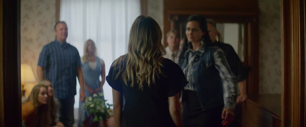 A young blonde woman walks into a room filled with people and hugs another woman