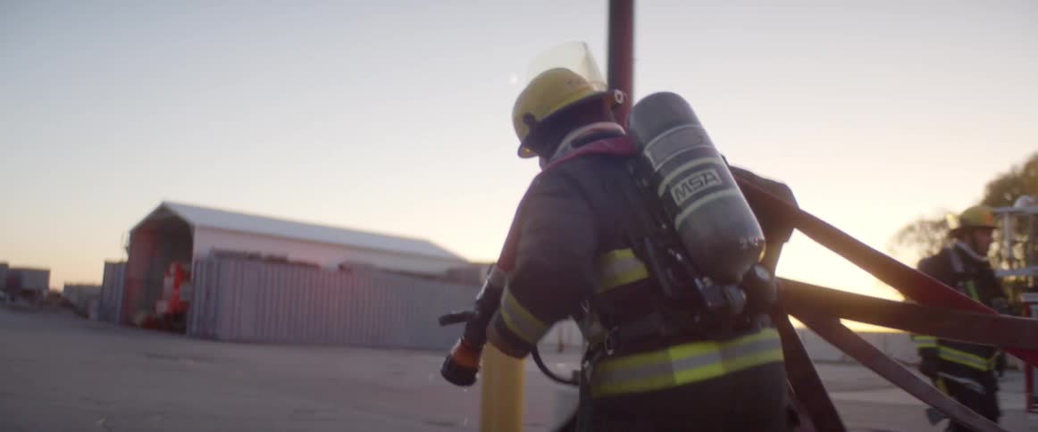 Fireman runs carrying empty fire hosewhile other firemen watch