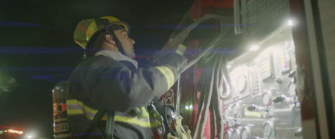 A firefighter in full gear unravels a hose thats folded up on a firetruck