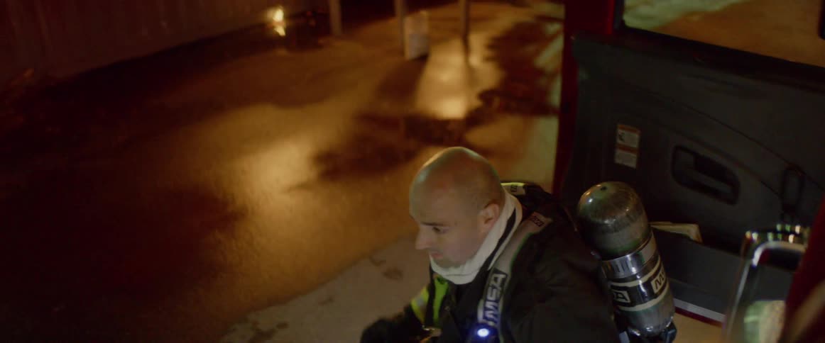 Firefighter exits fire engine and puts on protective gear near burning building