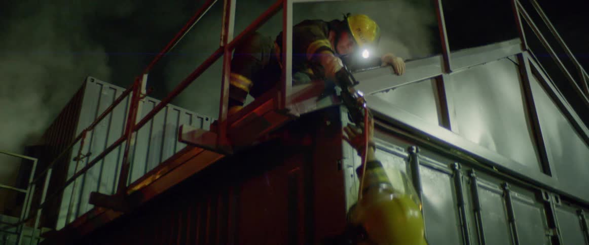 A firefighter passes a piece of equipment down to another firefighter