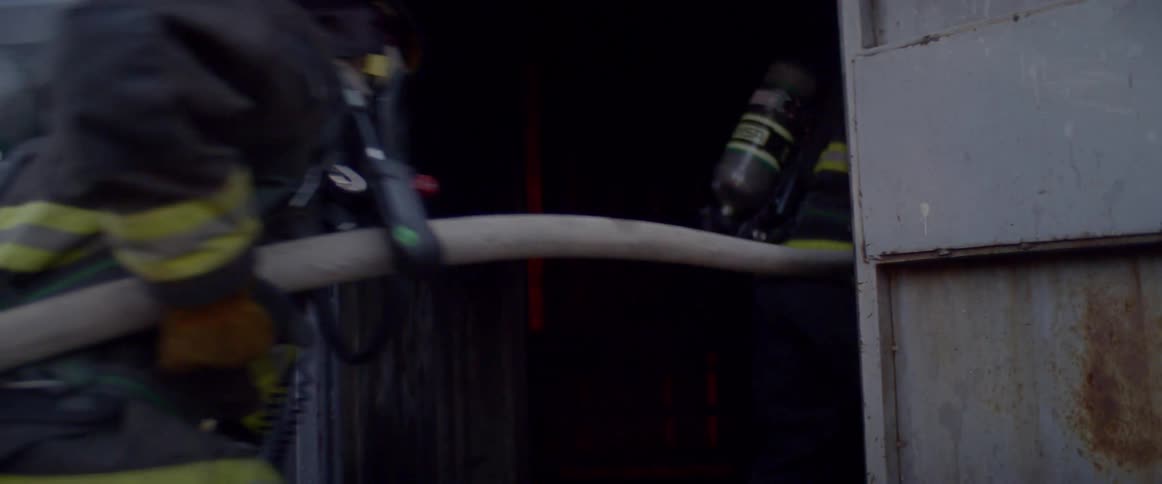 Two firefighters pull a fire hose through the open door of a building
