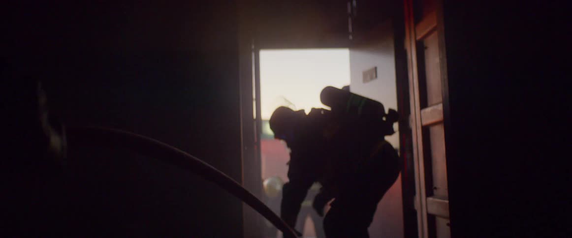 Two firemen pull fire hose into building in smoky atmosphere