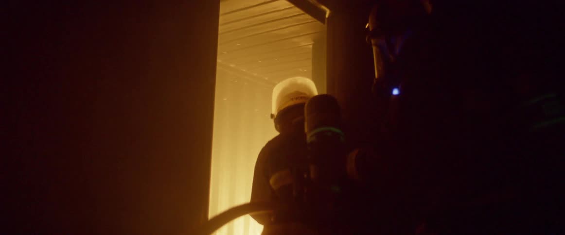 Firefighters carrying a hose enter a burning building