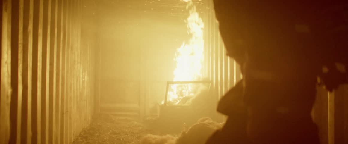 Firefighters walk through hallway with fire burning at the end